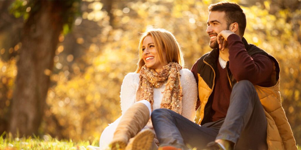 A couple sitting on the ground near trees in the autumn
