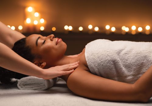 Therapist hands massaging young african lady shoulders at spa salon