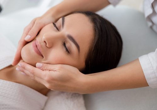 Relaxed young woman enjoying face massage at spa salon